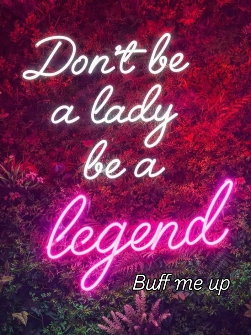 Neon sign on a wall of red flowers reading Don't be a lady, be a legend